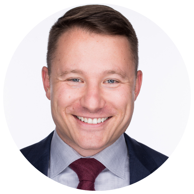 Professional headshot of a smiling man in a navy suit, light blue shirt, and burgundy tie against a light background
