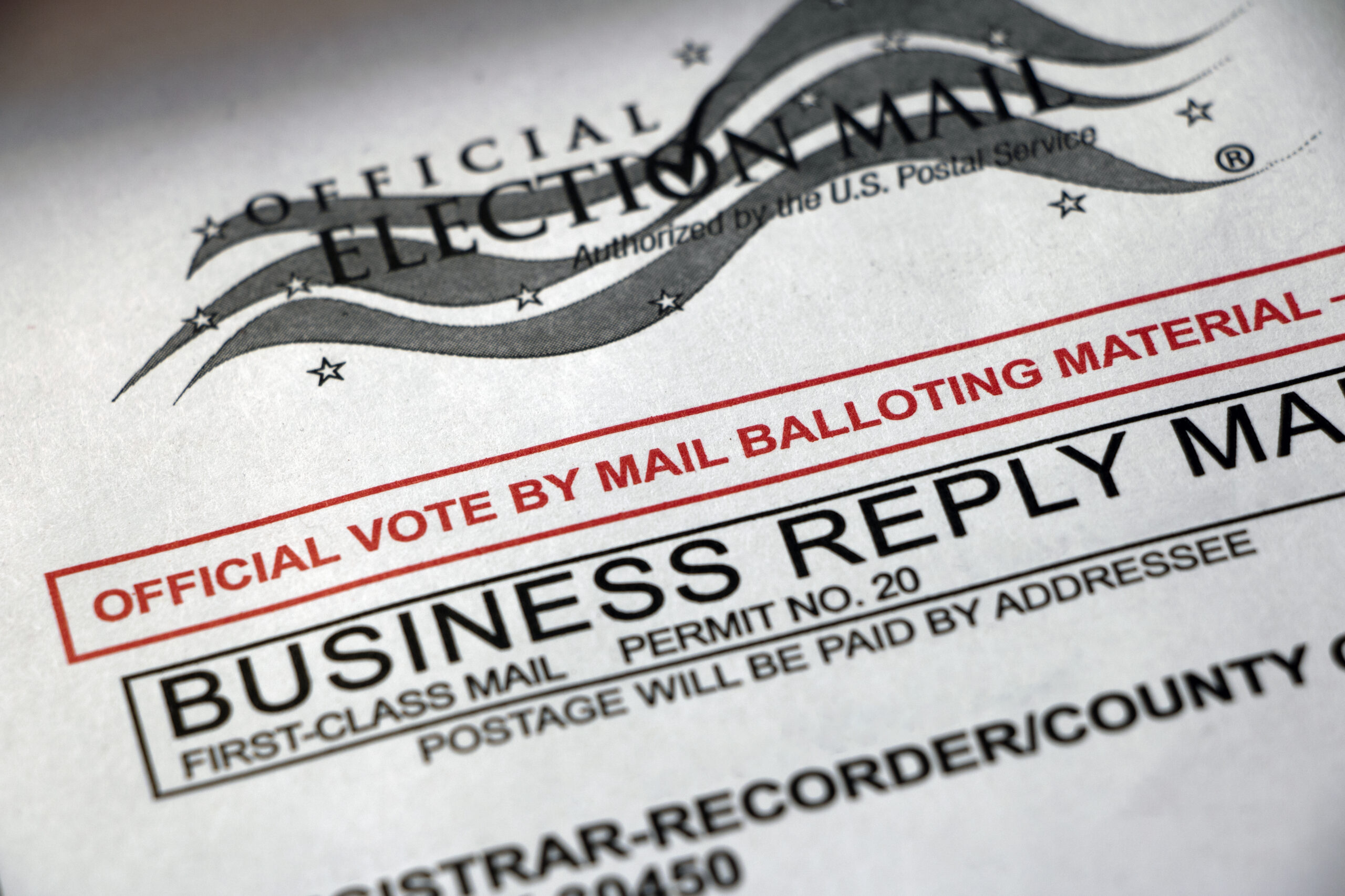 Close-up of an official election mail document showing 'Official Election Mail' and 'Business Reply Mail' labels with a red border.